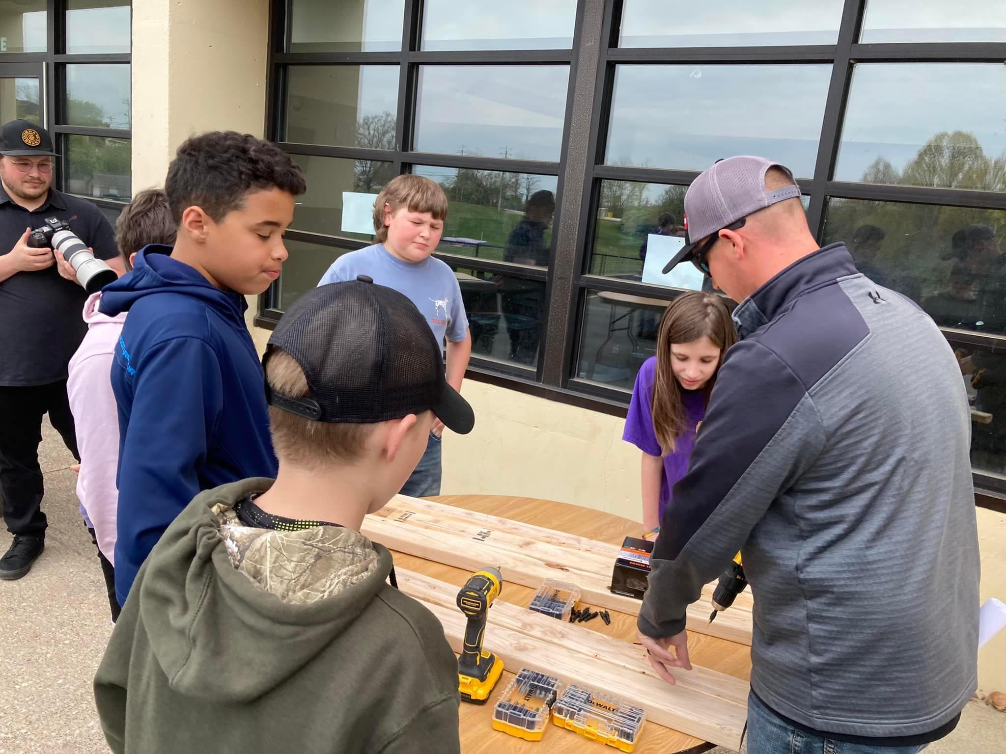 Campbell County Middle School students gather around a work table to practice using drills with a trades professional